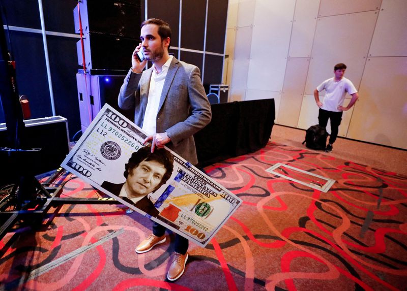 &copy; Reuters. FILE PHOTO: An assistant of Argentine congressman and presidential pre-candidate, Javier Milei, holds a giant US dollar bill with the face of Milei, before the presentation of Milei's book "El fin de la inflacion" (The End of the Inflation), at the Buenos