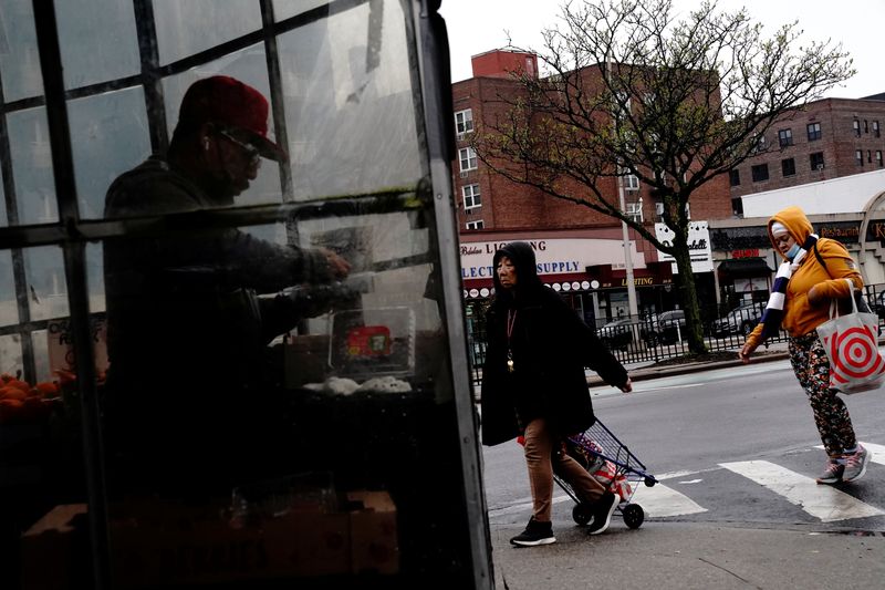 &copy; Reuters. Des piétons traversent la rue alors qu'un homme trie des baies à l'intérieur d'une épicerie à Forest Hills, dans le Queens à New York, États-Unis. /Photo prise le 2 mai 2022/REUTERS/Bing Guan