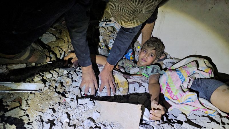 © Reuters. Palestinos trabajan para rescatar a un niño atrapado entre los escombros tras un ataque israelí contra una casa en Jabalia, en el norte de la Franja de Gaza. 19 de octubre de 2023. REUTERS/Anas al-Shareef     