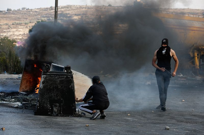 &copy; Reuters. شاب فلسطيني يختبئ خلف صندوق للقمامة خلال اشتباكات مع القوات الإسرائيلية قرب رام الله بالضفة الغربية في يوم 18 أكتوبر تشرين الأول 2023 . تصوير : 