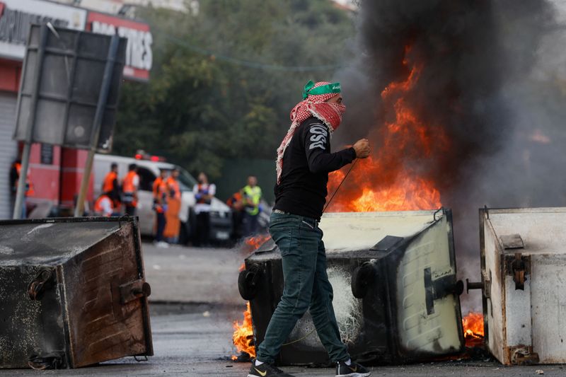 © Reuters. شاب فلسطيني يقف بجانب حرائق مشتعلة خلال اشتباكات مع القوات الإسرائيلية قرب رام الله بالضفة الغربية في يوم 18 أكتوبر تشرين الأول 2023 . 