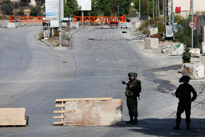 © Reuters. جنديان إسرائيليان يحرسان طريقا مغلقا بعد إغلاق مدينة الخليل بالضفة الغربية المحتلة في الثامن من أكتوبر تشرين الأول 2023 . تصوير : موسى قواسمة - رويترز .   