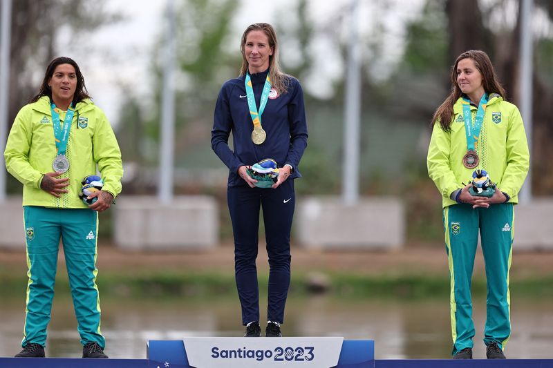 © Reuters. Pan-Am Games - Santiago 2023 - Open Water Swimming - Laguna Los Morros, Santiago, Chile - October 29, 2023 Gold medallist Ashley Twichell of the U.S. celebrates on the podium with silver medallist Brazil's Ana Marcela Cunha and bronze medallist Brazil's Viviane Jungblut during the women's 10km final medal ceremony REUTERS/Luisa Gonzalez