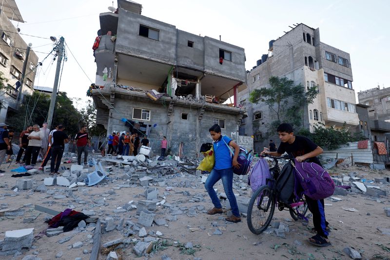 © Reuters. Young Palestinians walk in front of a damaged house in the aftermath of Israeli strikes in Khan Younis in the southern Gaza Strip, October 30, 2023. REUTERS/Mohammed Salem 