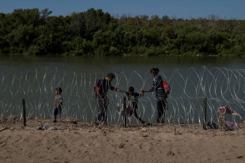© Reuters. FILE PHOTO: A family navigates the bank of the Rio Grande past razor wire while searching for an entry point into the United States from Mexico, in Eagle Pass, Texas, U.S. July 30, 2023.  REUTERS/Adrees Latif/File Photo