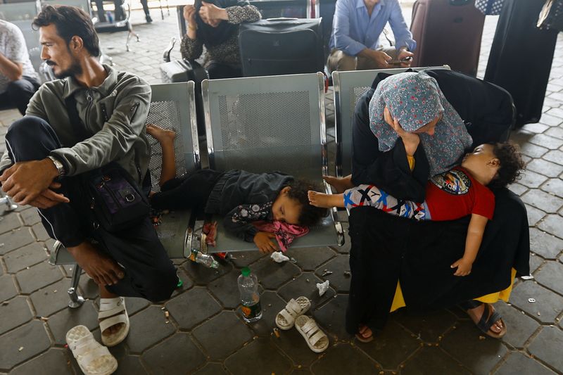 &copy; Reuters. امرأة فلسطينية، تحمل جواز سفر مصريا، تجلس مع أطفالها أثناء انتظارهم الحصول على تصريح لمغادرة غزة عند معبر رفح الحدودي مع مصر في رفح بجنوب قط