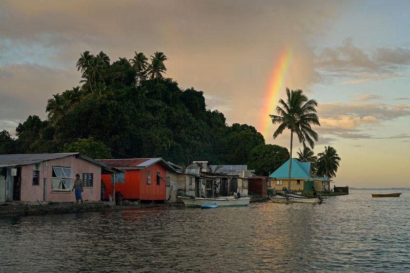© Reuters. FILE PHOTO: Local resident Tarusila Boseiwaqa walks along a sea wall that no longer protects homes from the intrusion of water at higher tides, as a rainbow forms over Serua Village, Fiji, July 14, 2022. REUTERS/Loren Elliott/File Photo