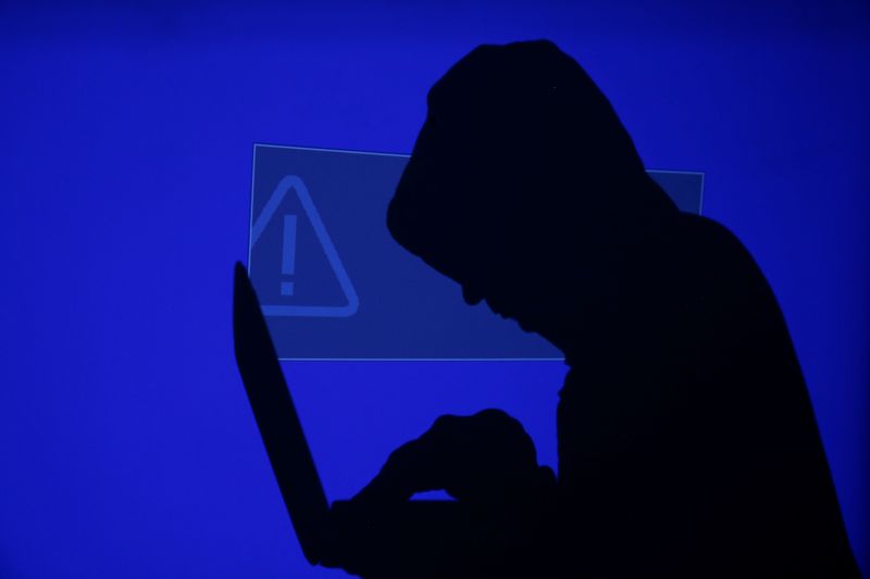 © Reuters. A hooded man holds a laptop computer as blue screen with an exclamation mark is projected on him in this illustration picture taken on May 13, 2017. REUTERS/Kacper Pempel/Illustration