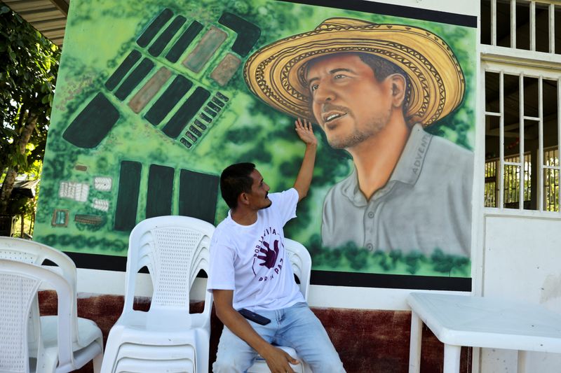 © Reuters. Armando Aroca, environmentalist, former guerrilla and signatory of the peace agreement between the Revolutionary Armed Forces of Colombia (FARC) and the Colombian government, and current nursery manager of the Common Community Multi Active Cooperative (COMUCCOM) farm, points to a mural with the image of Jorge Santofimio, a murdered environmentalist and former guerrilla member and signatory of the peace agreement between the Revolutionary Armed Forces of Colombia (FARC) and the Colombian government, in Puerto Guzman, Colombia June 27, 2023. REUTERS/Luisa Gonzalez