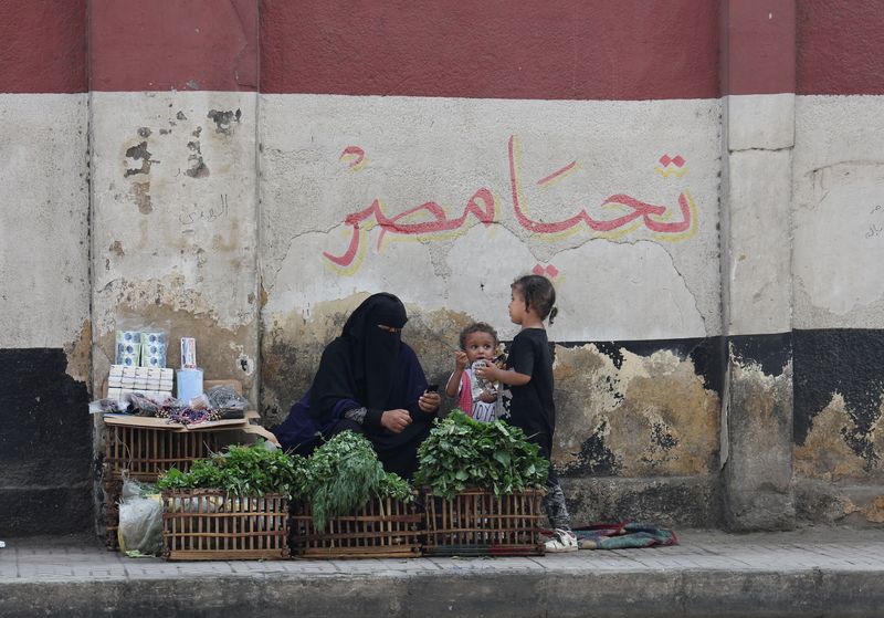 &copy; Reuters. بائعة متجولة مع أطفالها تجلس أمام لوحة جدارية عليها العلم الوطني المصري ومكتوب عليه "تحيا مصر" يوم 10 نوفمبر تشرين الثاني 2023. تصوير: عمرو عبدا