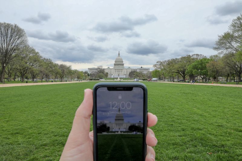 © Reuters. FILE PHOTO: A mobile phone showing the time at noon, is displayed for a photo in front of the United States Capitol, in Washington, U.S., March 31, 2020. REUTERS/Jonathan Ernst/File Photo