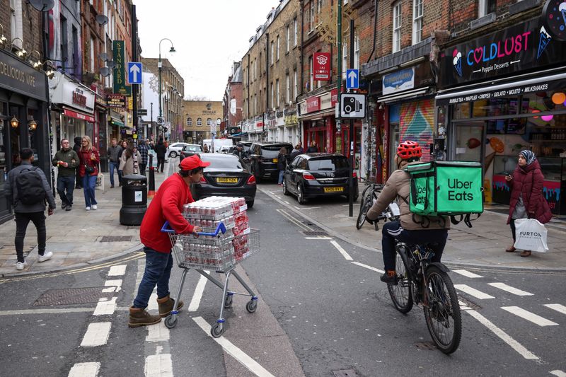 &copy; Reuters. A man pushes a trolly of Coke cans as an Uber Eats rider passes by in Brick Lane in London, Britain, April 1, 2023.   REUTERS/Kevin Coombs