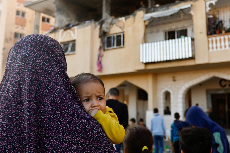 &copy; Reuters. Una mujer con un bebé en brazos en el lugar de un ataque israelí contra un edificio de apartamentos, en medio del conflicto entre Israel y el grupo islamista palestino Hamás, en Jan Yunis, en el sur de la Franja de Gaza. 18 de noviembre, 2023. REUTERS/