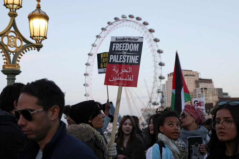 © Reuters. A demonstrator holds a placard, as people cross the Westminster Bridge, during a protest in solidarity with Palestinians in Gaza, during a temporary truce between the Palestinian Islamist group Hamas and Israel, in London, Britain, November 25, 2023. REUTERS/Hollie Adams    