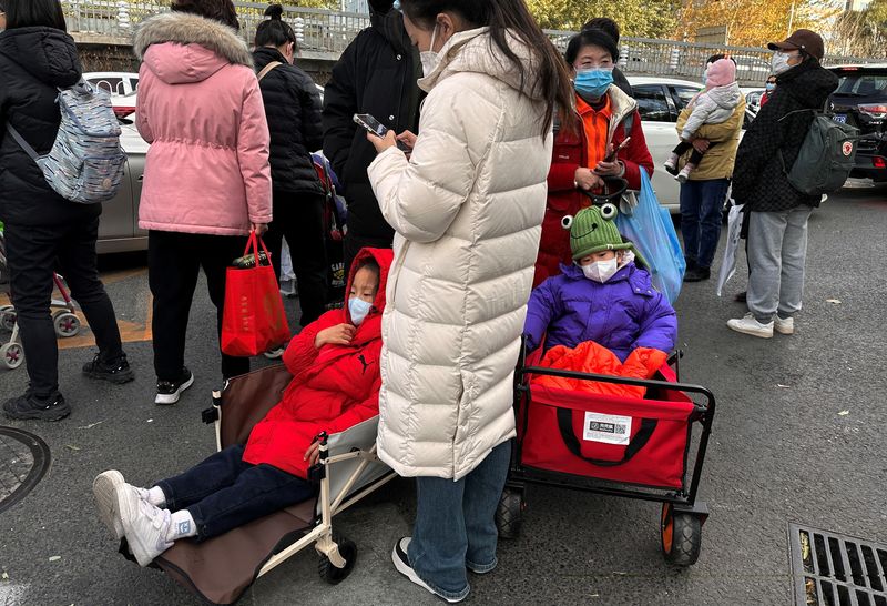 &copy; Reuters. FILE PHOTO: People stand next to children sitting in camping carts as they wait for their rides outside a children's hospital in Beijing, China November 27, 2023. REUTERS/Tingshu Wang/File Photo