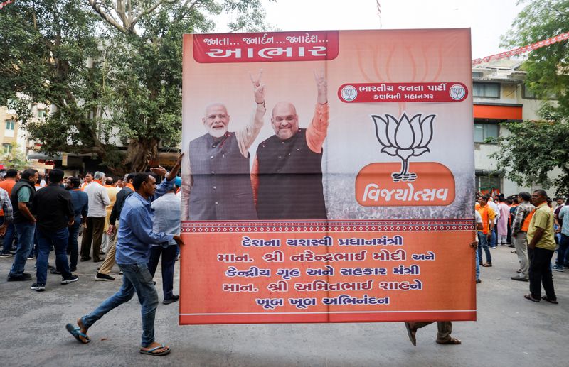 © Reuters. FILE PHOTO: Supporters of India's ruling Bharatiya Janata Party (BJP) carry a hoarding of Indian Prime Minister Narendra Modi and Union Minister of Home Affairs Amit Shah for celebrations after winning three out of four states in key regional polls outside the party headquarters in Ahmedabad, India, December 3, 2023.REUTERS/Amit Dave/File Photo