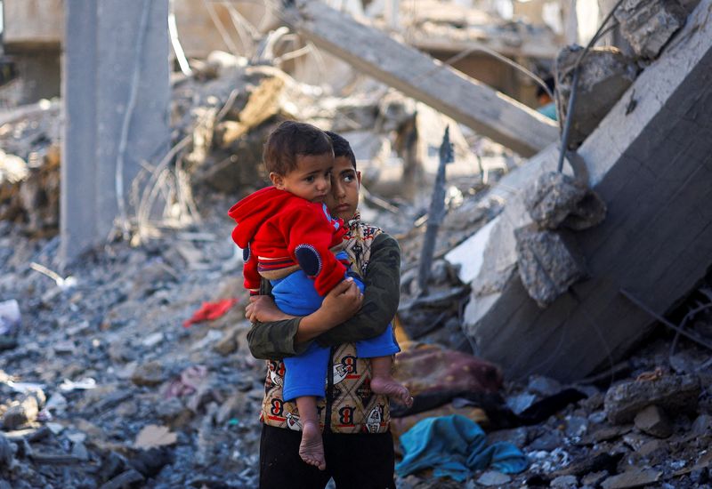 © Reuters. Un niño palestino con un bebé en brazos en un lugar donde hubo ataques israelíes, en medio del actual conflicto entre Israel y el grupo palestino Hamás, en Rafah, en el sur de la Franja de Gaza. 4 de diciembre de 2023. REUTERS/Mohammed Salem  