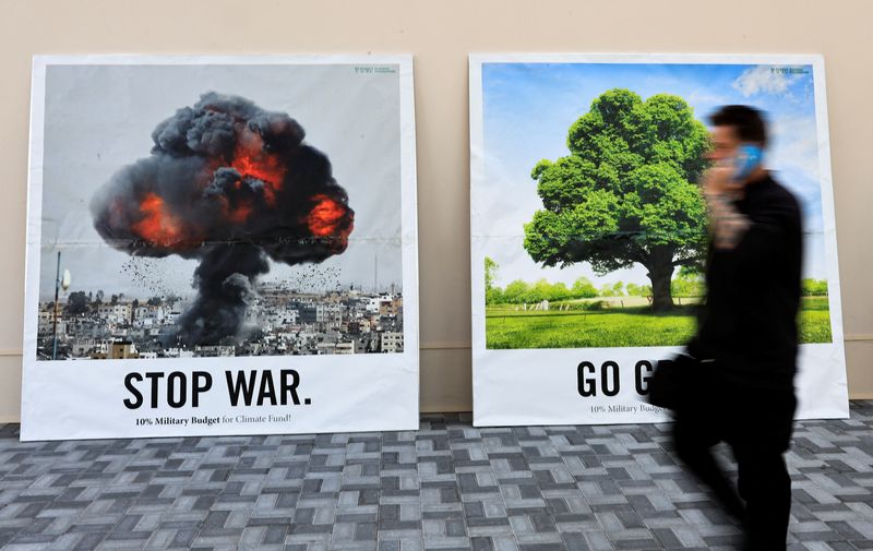 &copy; Reuters. Un hombre pasa junto a un muro con dos pancartas en las que se puede leer "Stop war" y "Go green" en la Conferencia de las Naciones Unidas sobre el Cambio Climático (COP28) en Dubai, Emiratos Árabes Unidos. 8 de diciembre de 2023. REUTERS/Thaier Al Suda