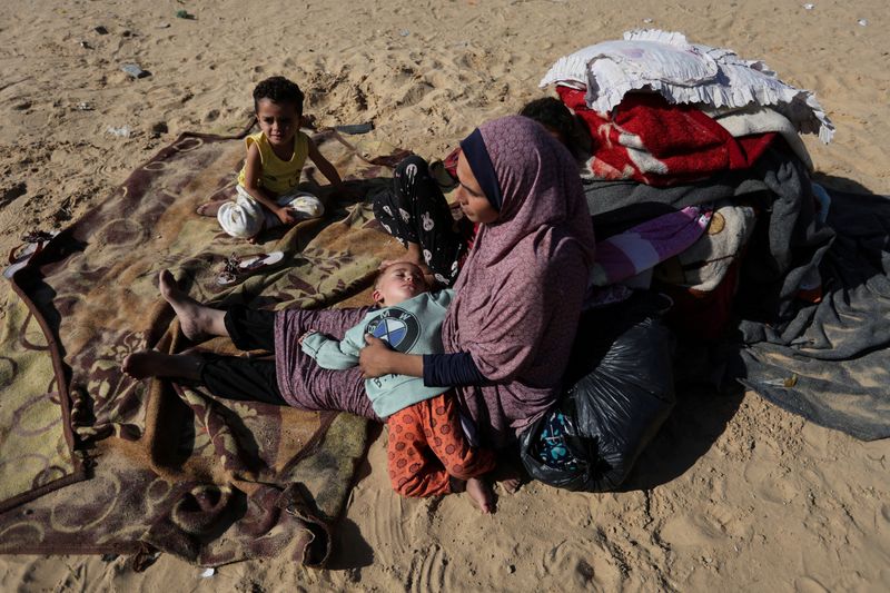 &copy; Reuters. Foto de archivo de una mujer sentada con sus hijos al aire libre, mientras los palestinos desplazados, que huyeron de sus casas debido al ataque israelí, se refugian en un campamento en Rafah, en medio del actual conflicto entre Israel y el grupo islamis