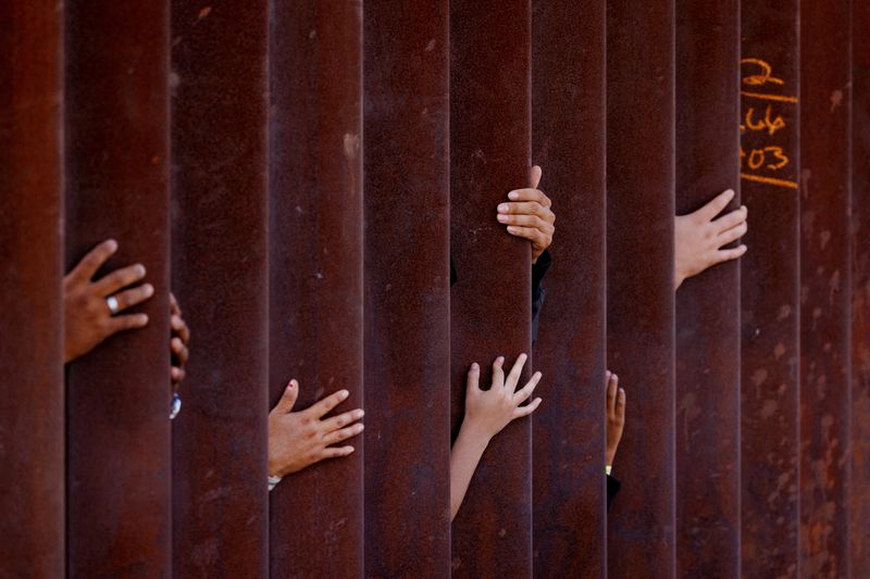 &copy; Reuters. FILE PHOTO: Migrants wait for some food from an aid worker after gathering between the primary and secondary border fences between Mexico and the United States as they await processing by U.S immigration in San Diego, U.S., September 12, 2023. REUTERS/Mik