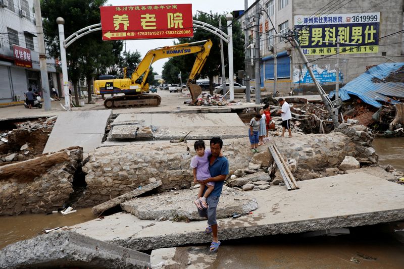 &copy; Reuters. FILE PHOTO: A man holding a child walks across a damaged bridge after the rains and floods brought by remnants of Typhoon Doksuri, in Zhuozhou, Hebei province, China August 7, 2023. REUTERS/Tingshu Wang/File Photo