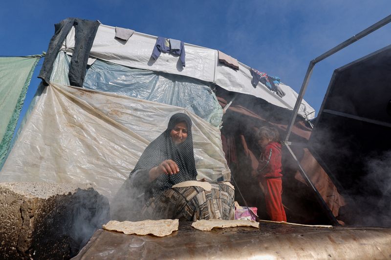 &copy; Reuters. A child stands next to a cooking woman, as displaced Palestinians, who fled their houses due to Israeli strikes, shelter in a tent camp near the border with Egypt, amid the ongoing conflict between Israel and the Palestinian Islamist group Hamas, in Rafah