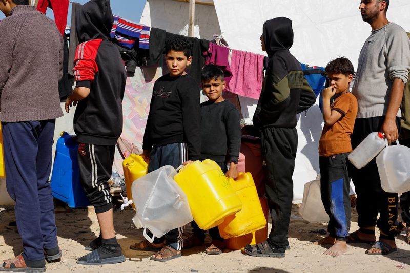 &copy; Reuters. FOTO DE ARCHIVO: Chicos palestinos sosteniendo bidones mientras hacen cola, mientras los palestinos desplazados, que huyeron de sus casas debido a los ataques israelíes, se refugian en un campamento de tiendas de campaña cerca de la frontera con Egipto,