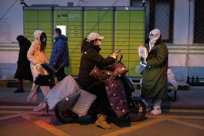 &copy; Reuters. 　１２月１４日、中国が新型コロナウイルスの感染を徹底的に封じ込める「ゼロコロナ政策」を解除してから１年余りが経過した。写真は、防護服を着た予防担当者に証明書を提示し、居住