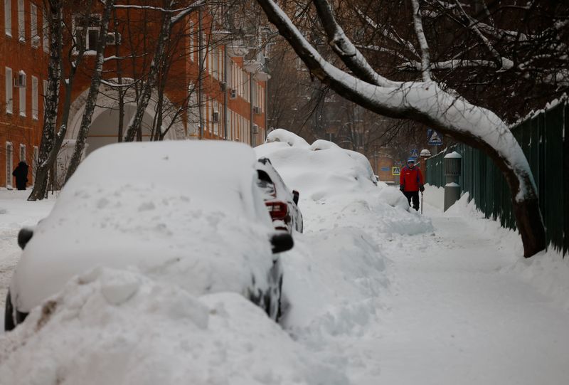 &copy; Reuters. رجل يسير أمام سيارات مغطاة بالثلوج بعد تساقط الثلوج بكثافة في موسكو يوم الجمعة. تصوير: مكسيم شيميتوف - رويترز.