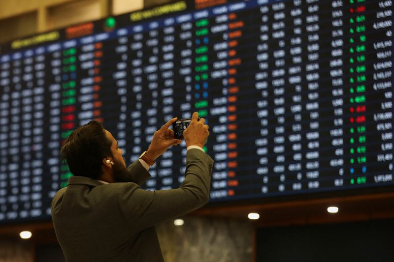 &copy; Reuters. FILE PHOTO: A man uses a mobile phone as he takes a photo of the electronic board displaying share prices during a trading session at the Pakistan Stock Exchange, in Karachi, Pakistan November 28, 2023. REUTERS/Akhtar Soomro