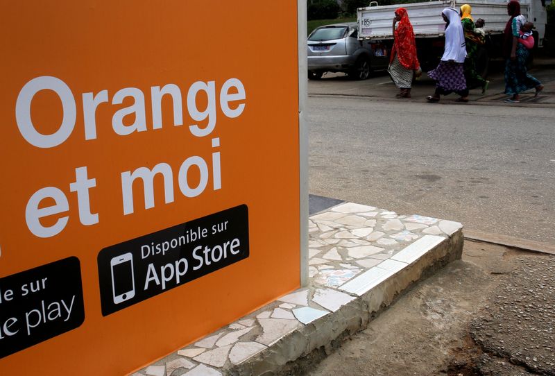 &copy; Reuters. Des personnes marchent à côté d'un kiosque Orange money, alors qu'Orange lance ses premiers services Orange Bank à Abidjan, en Côte d'Ivoire. /Photo d'archive/REUTERS/Luc Gnago