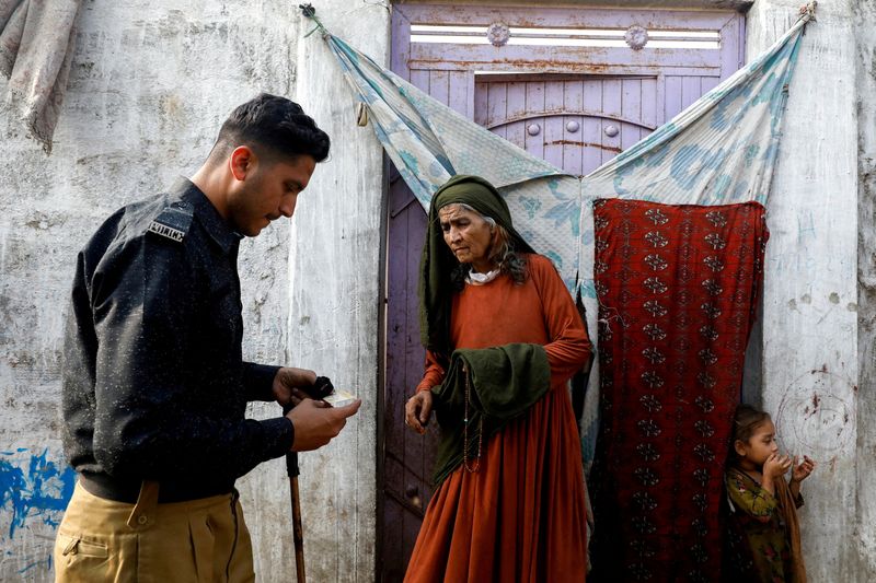 &copy; Reuters. أفغانية تقف عند مدخل منزلها بينما يفحص ضابط شرطة بطاقة تسجيلها خلال حملة تفتيش علي المواطنين الأفغان غير المسجلين في مخيم للأفغان بكراتشي ف