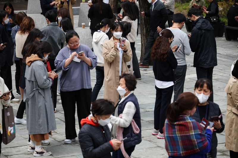 &copy; Reuters. FILE PHOTO: Office workers look at their mobile phones to check the local online banking app Toss as they gather at Seoul Museum of Art during a lunch break in Seoul, South Korea, April 13, 2023.  REUTERS/Kim Hong-Ji/File Photo