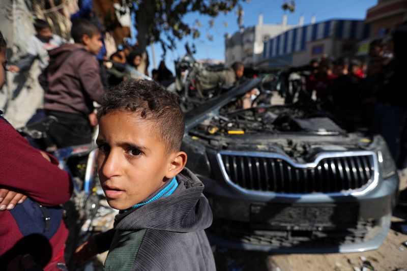 &copy; Reuters. Children watch as Palestinians inspect the remains of a car where Palestinian journalist Hamza Al-Dahdouh was killed along with another journalist in an Israeli strike, in Rafah in the southern Gaza Strip, January 7, 2024. REUTERS/Ibraheem Abu Mustafa