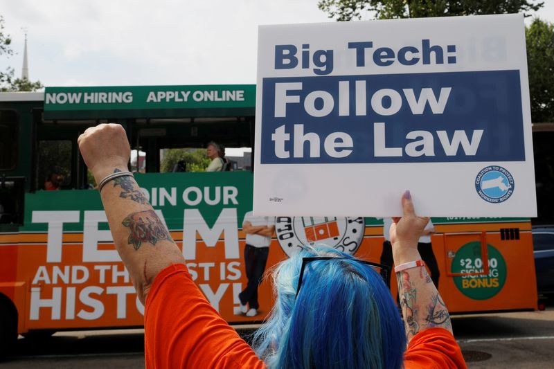 © Reuters. Mary Garcia, from New England United 4 Justice, gestures to a tour bus and holds a sign reading “Big Tech Follow the Law” at a demonstration opposing a ballot campaign by companies such has Uber, Lyft and Door Dash to exempt their companies from some labor laws outside the Massachusetts Statehouse in Boston, Massachusetts, U.S., June 22, 2021.   REUTERS/Brian Snyder