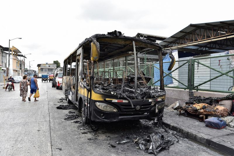 &copy; Reuters. أشخاص يسيرون بجوار حافلة محترقة في جواياكيل بالإكوادور يوم الثلاثاء. تصوير: فيسنتي جايبور ديل بينو - رويترز.
