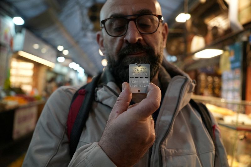 © Reuters. Steven Winston, a visitor from Britain, holds up a military-style dog tag calling for the return of Israeli hostages who have been held in the Gaza Strip since they were seized by Hamas gunmen on October 7, at Mahane Yehuda market in Jerusalem, January 11, 2024. The Hebrew reads 