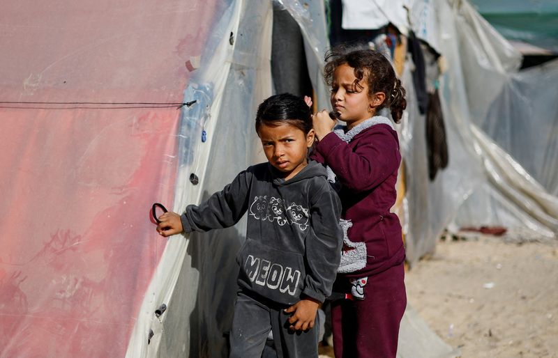 &copy; Reuters. Una niña palestina desplazada, que huyó de su casa debido a los ataques israelíes, ayudando a otra niña con su pelo, en medio del conflicto en curso entre Israel y el grupo islamista palestino Hamás, dentro de un campamento de tiendas de campaña en 