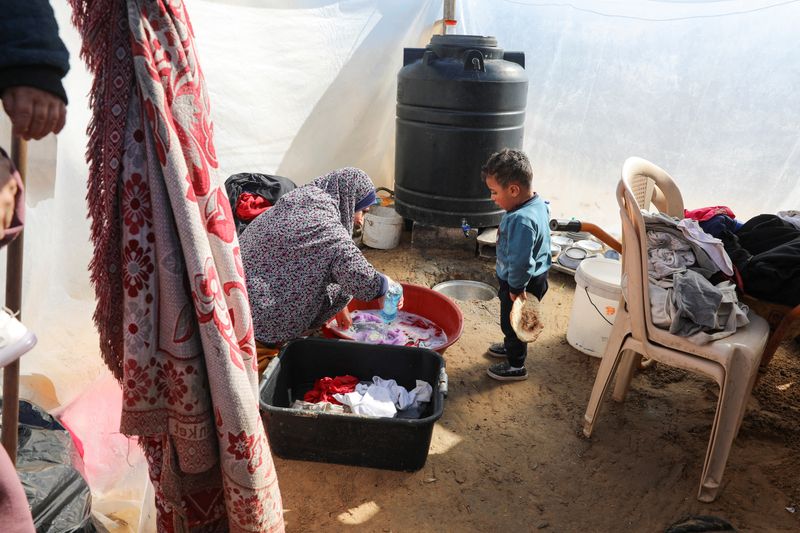 &copy; Reuters. امرأة فلسطينية تغسل الملابس ويقف صبي يحمل الخبز بجانبها، بينما يواجه سكان غزة مستويات أزمة الجوع وسوء التغذية المتزايد، في خان يونس بجنوب ق
