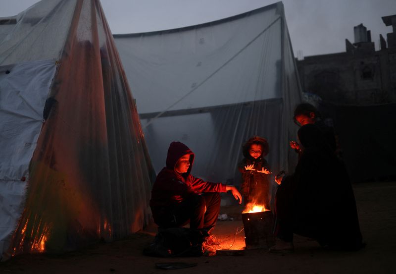 &copy; Reuters. Palestinos deslocados, que fugiram de suas casas devido aos ataques israelenses, se aquecem perto de fogueira em dia chuvoso e frio em um acampamento, em Rafah
26/01/2024
REUTERS/Saleh Salem    