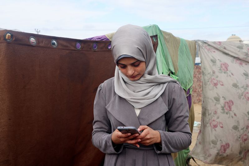 &copy; Reuters. Aseel Abu Haddaf, a Palestinian medical student who fled her house in Khan Younis with her family due to Israeli strikes amid the ongoing conflict between Israel and the Palestinian Islamist group Hamas, uses her mobile phone at a tent camp where they she