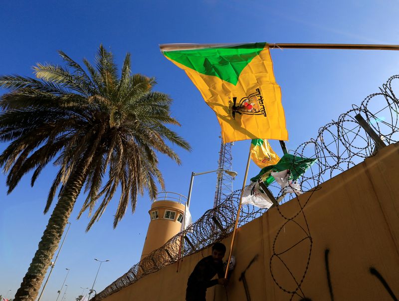 © Reuters. FILE PHOTO: A member of Hashd al-Shaabi (paramilitary forces) holds a flag of the Kataib Hezbollah militia group during a protest to condemn air strikes on their bases, outside the main gate of the U.S. Embassy in Baghdad, Iraq December 31, 2019. REUTERS/Thaier al-Sudani/File Photo