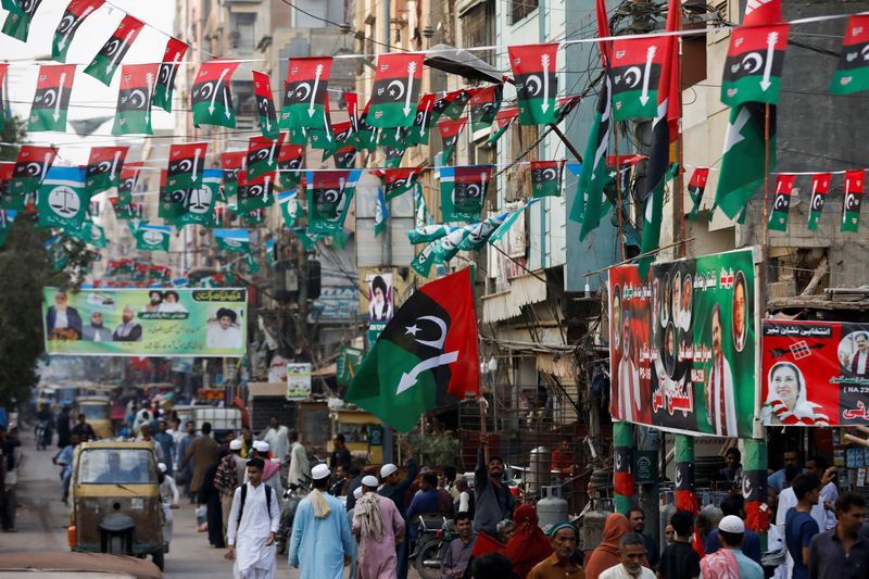 &copy; Reuters. أشخاص يسيرون في شارع مزين بأعلام الحملات الانتخابية وملصقات الأحزاب السياسية قبل الانتخابات العامة في كراتشي بباكستان يوم 23 يناير كانون ال