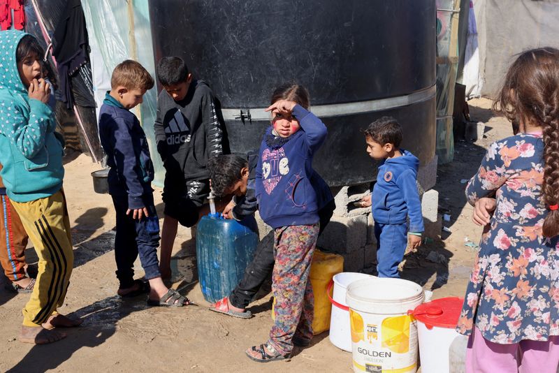 &copy; Reuters. Refugiados niños palestinos desplazados, que huyeron de sus casas debido a los bombardeos israelíes, esperando para recoger agua en medio de la escasez, en un campamento de tiendas de campaña en Ráfah, en el sur de la Franja de Gaza. 1 de febrero de 2