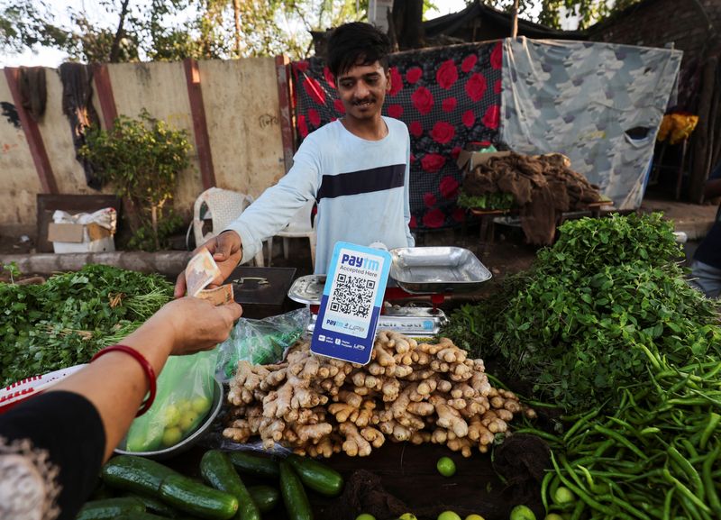 &copy; Reuters. A customer pays cash to buy vegetables next to a QR code of Paytm, a digital payments firm, on display at a roadside market in Ahmedabad, India, February 5, 2024.REUTERS/Amit Dave