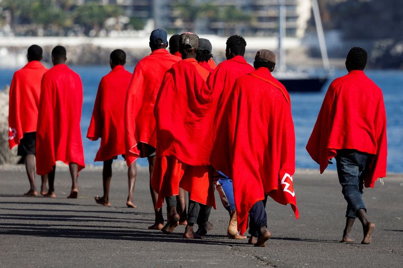 © Reuters. Un gruppo di migranti cammina nel porto di Arguineguin per essere assistito dalla Croce Rossa dopo essere sbarcato da una nave della guardia costiera spagnola, nell'isola di Gran Canaria, Spagna, 12 ottobre 2023. REUTERS/Borja Suarez