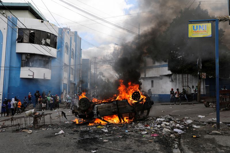 © Reuters. People stand near a car set ablaze by demonstrators to block the route of Haitian National Police officers trying to get to the scene where agents of Haiti's BSAP, an armed environmental agency that has in recent years evolved into a paramilitary body, were killed in a shootout with security forces, in Port-au-Prince, Haiti, February 7, 2024. REUTERS/Ralph Tedy Erol