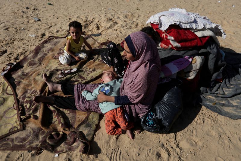 &copy; Reuters. Una mujer sentada con sus hijos al aire libre, mientras los palestinos desplazados, que huyeron de sus casas debido al ataque israelí, se refugian en un campamento en Ráfah, en medio del conflicto en curso entre Israel y el grupo islamista palestino Ham