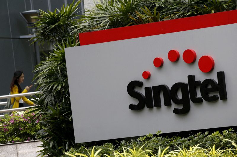 &copy; Reuters. FILE PHOTO: A woman using a mobile phone walks behind a Singtel signage at their head office in Singapore February 11, 2016.  REUTERS/Edgar Su/File Photo