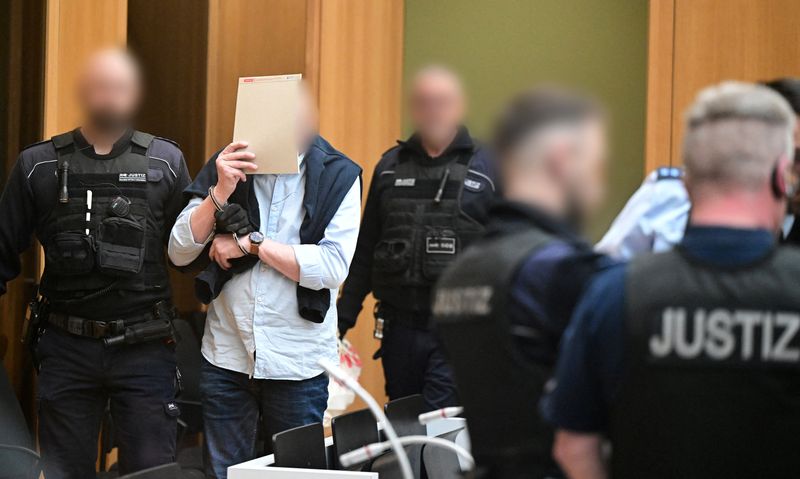 © Reuters. A defendant in handcuffs arrives in a courtroom were nine men go on trial charged with high treason, attempted murder and plotting a violent coup d'etat aimed at installing an aristocrat as national leader and imposing martial law, in Stuttgart, Germany, April 29, 2024. The hearing marks the start of three marathon trials of 27 people in total, including Heinrich XIII Prinz Reuss, accused of conspiring in a plot foiled by authorities at the end of 2022. Monday's trial focuses on nine suspects, members of the Reichsbuerger (Citizens of the Reich) group, who allegedly aimed to impose harsh military law on Germany after carrying out a coup.    Bernd Weißbrod/Pool via REUTERS